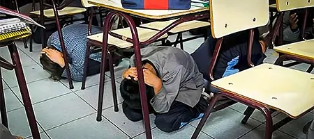 Niños debajo de su pupitre, hincados y con las manos protegiendo su cabeza Niños debajo de su pupitre, hincados y con las manos protegiendo su cabeza