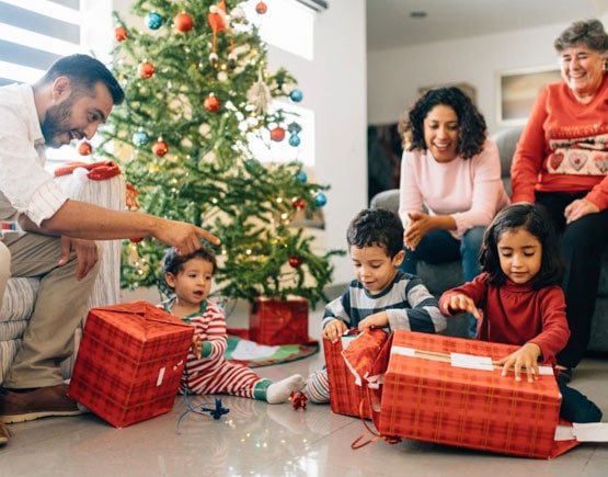 Niños sonriendo abriendo sus regalos de Navidad en compañía de sus padres Familia compartiendo la cena de nochebuena frente al árbol de Navidad
