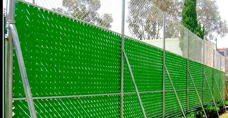 Reja de acero siendo equipada con cinta rompevientos y coronada con alambre de púas o concertina para mayor seguridad de una casa Reja de acero siendo equipada con cinta rompevientos y coronada con alambre de púas o concertina para mayor seguridad de una casa