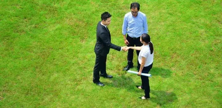 Personas de negocios estrechando las manos en medio de un terreno en venta Personas de negocios estrechando las manos en medio de un terreno en venta