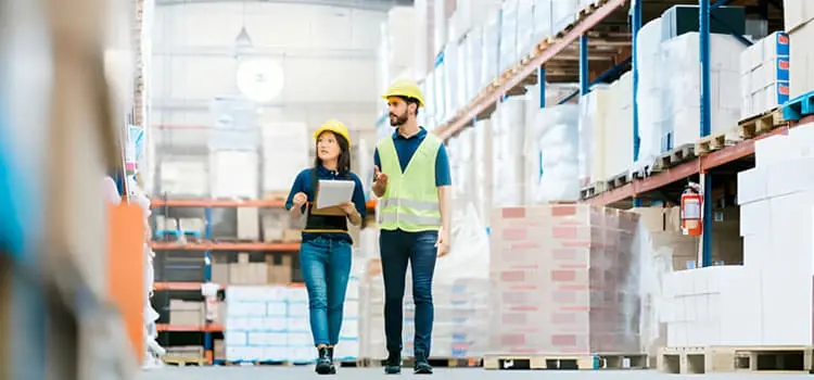 Mujer y hombre caminando entre grandes estantes industriales con diversas mercancías Mujer y hombre caminando entre grandes estantes industriales con diversas mercancías