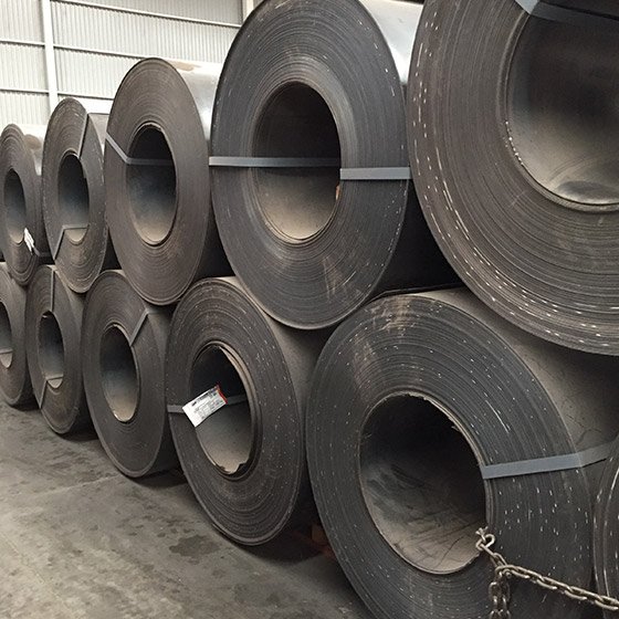 Rollos de lamina negra acomodados horizontalmente unos sobre otros dentro de una bodega