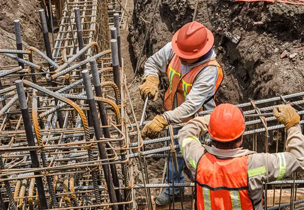 Trabajadores con equipo de seguridad amarrando varillas con alambre recocido