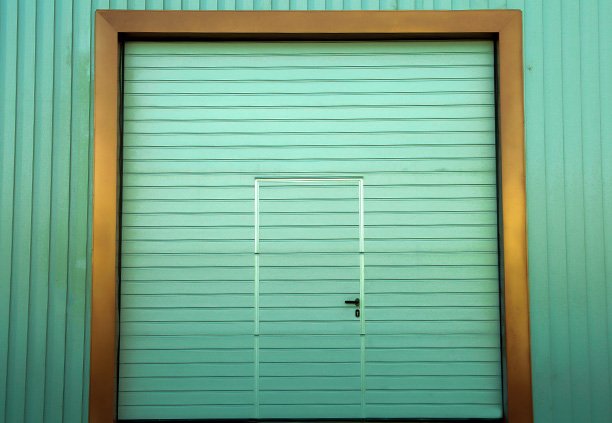 Una cortina de acero verde con una puerta más pequeña en el medio, ambas elaboradas con Lámina tipo tablero, en un entorno industrial.