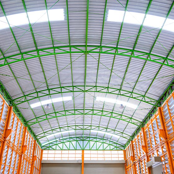 Vista del interior de una bodega hecha con Láminas Pintro y Perfiles de acero pintados de color verde y naranja.