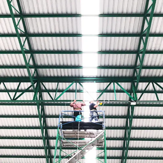 Dos personas en un andamio trabajando en labores de mantenimiento de un techo de bodega, hecho de perfiles de acero y lámina pintro