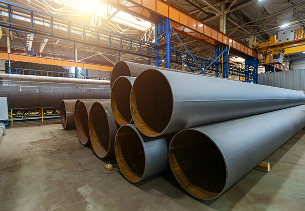 Tubos estructurales de lámina negra colocados sobre polines de madera dentro de una planta industrial