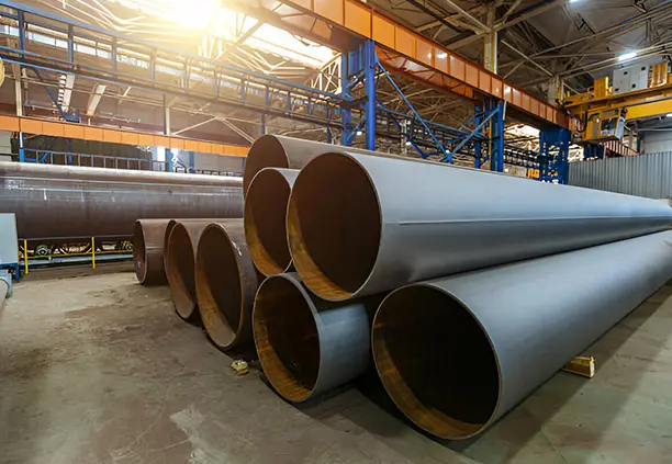 Tubos estructurales de lámina negra colocados sobre polines de madera dentro de una planta industrial