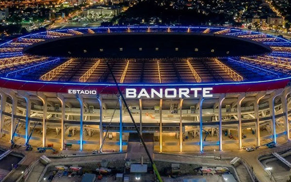 Vista aérea y nocturna del Estadio Banorte con sus columnas iluminadas de color amarillo y azul